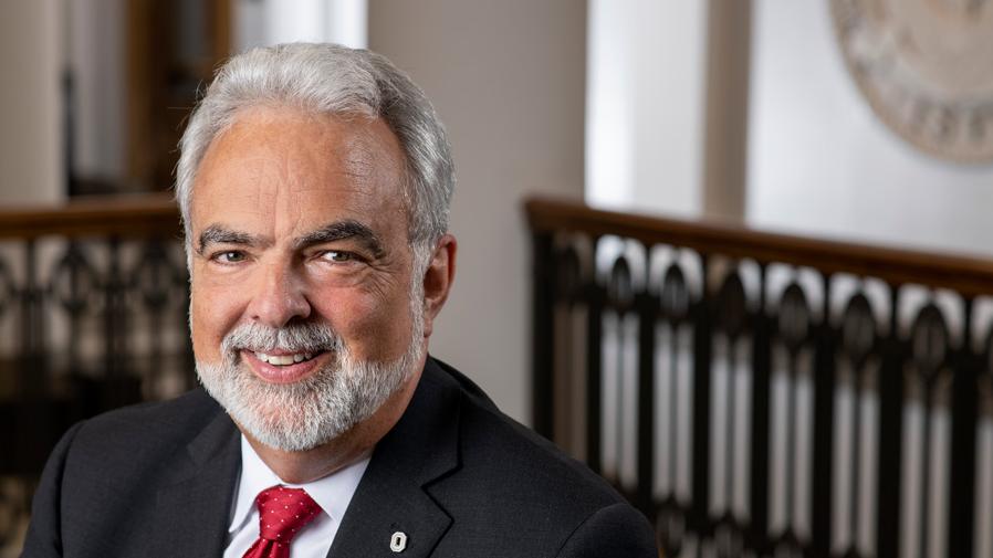 Portrait of Michael C. Eicher in front of the University Seal.