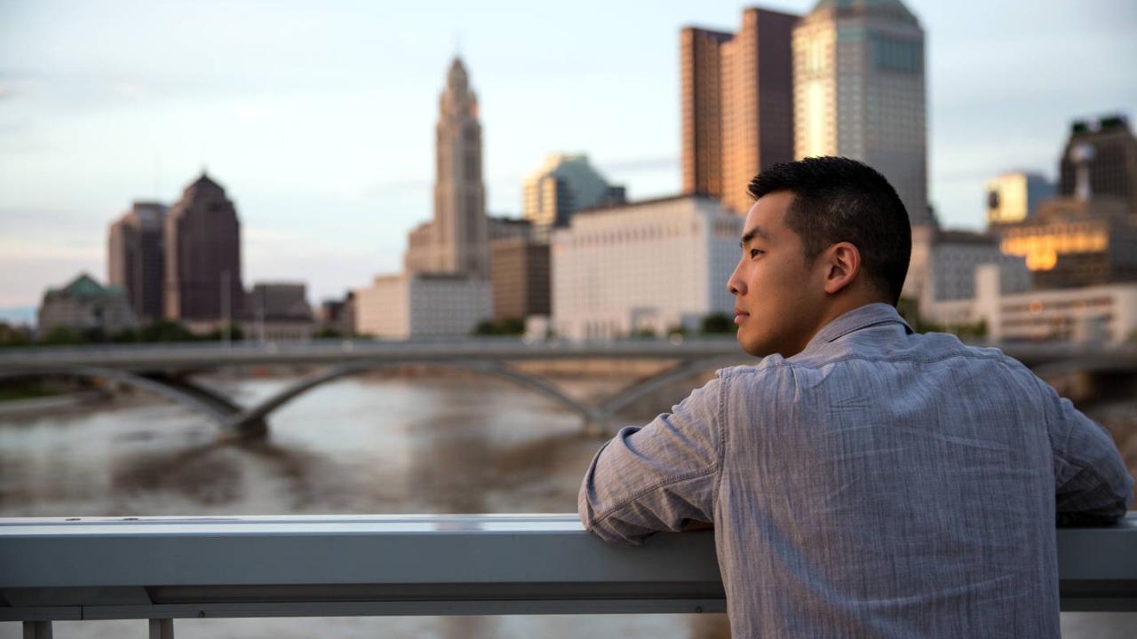 a man overlooking a river with the city of columbus and its skyscrapers on the horizon